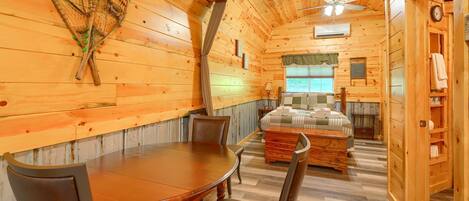 L’intérieur d’une cabane en bois comprend un coin repas, un lit et un ventilateur de plafond.