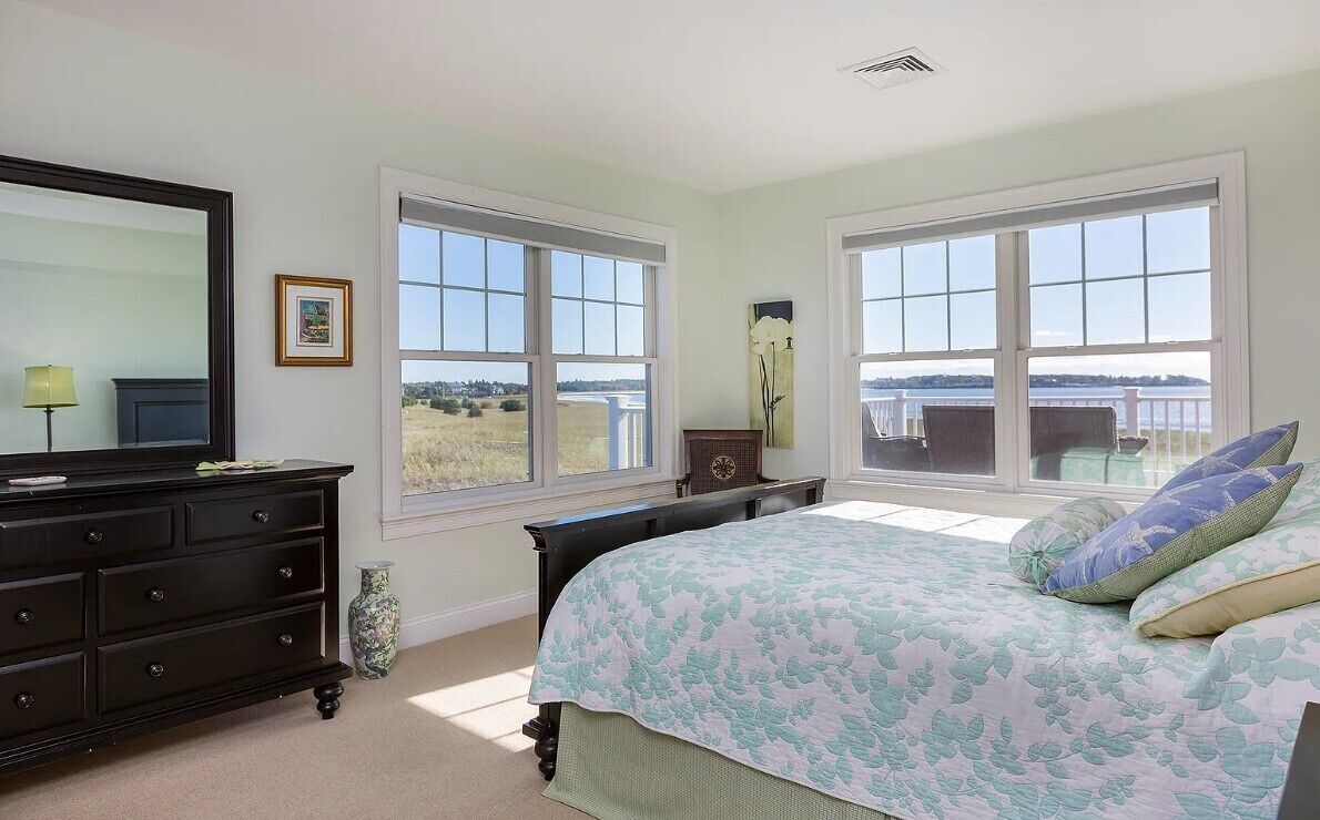 Un dormitorio con una cama grande, dos ventanas, un aparador y un espejo.