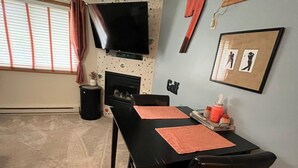Un comedor con una mesa y sillas negras, chimenea, televisor montado en la pared y un cuadro enmarcado con motivos de golf.