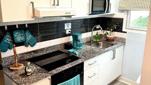 A modern kitchen with white cabinets, a black stove, a sink, and a microwave. There are teal kitchen towels hanging on the oven handle. - Charming, elegant 2-bedroom condo with WiFi, AC in delightful Playa Juan Dolio (Playa Juan Dolio)