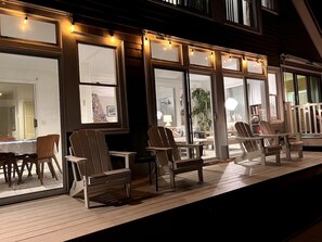 En udendørs terrasse med træstole og borde, store vinduer med lyskæder og udsigt til indretningen indeni.