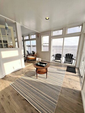 A spacious living room with large windows, a wooden floor, and a central coffee table.