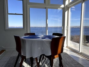 A dining area with a table set for four, large windows offering a view of the sea and a distant shoreline.