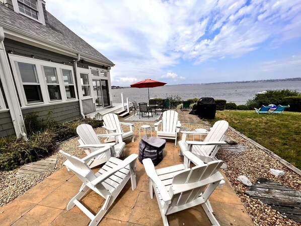 En terrasse med hvide Adirondack-stole, en rød parasol og en grill.