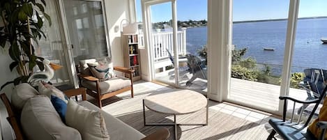 A spacious living room with a large window overlooking a body of water, a comfortable sofa, a coffee table, and a bookshelf.
