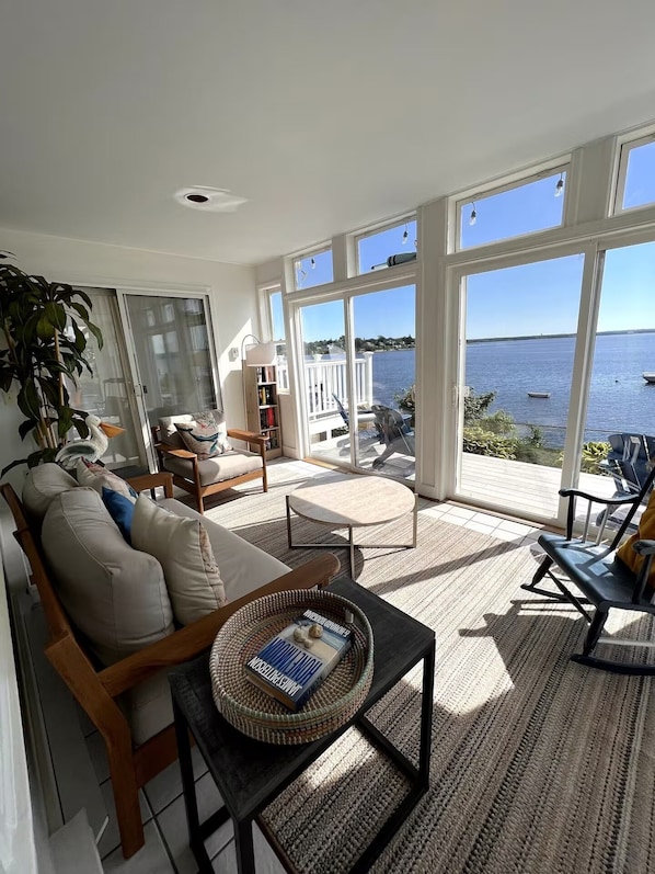 A spacious living room with a large window overlooking a body of water, a comfortable sofa, a coffee table, and a bookshelf.