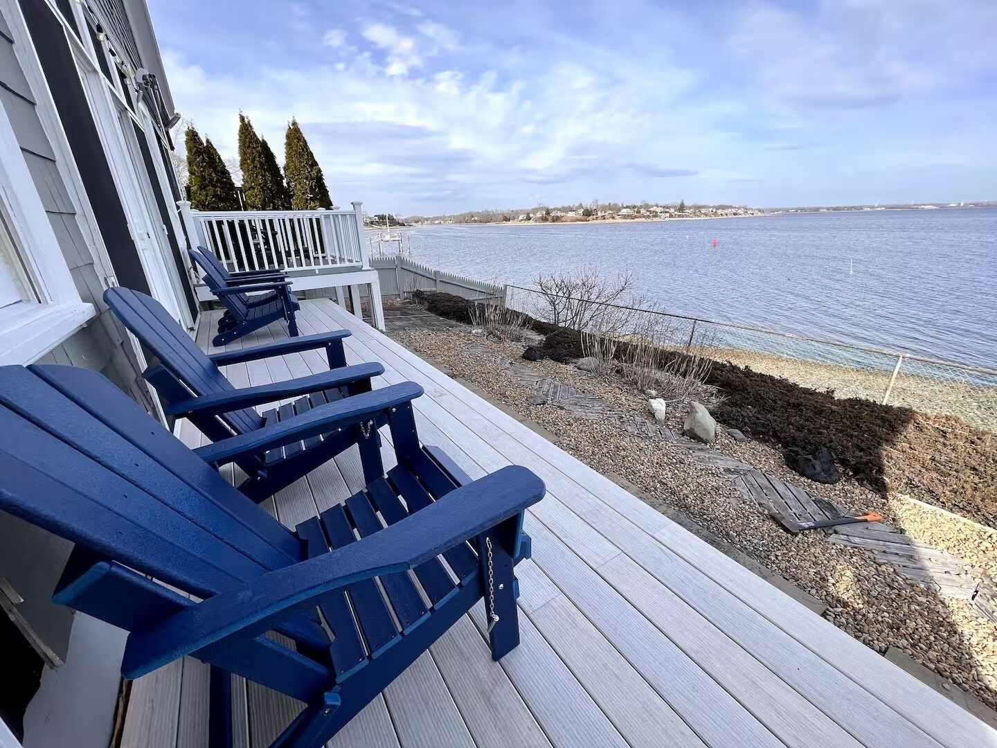Une terrasse en bois avec des chaises Adirondack bleues, donnant sur une étendue d’eau.