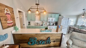 A kitchen with teal cabinets, a wooden island with a 'Beach' sign, and pendant lighting.