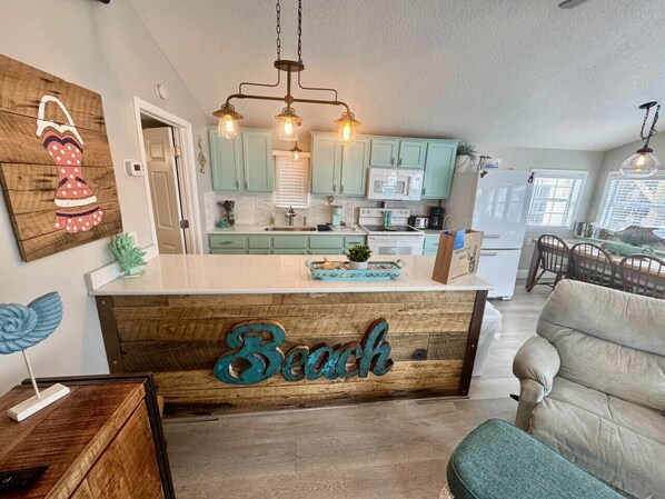 A kitchen with teal cabinets, a wooden island with a 'Beach' sign, and pendant lighting.