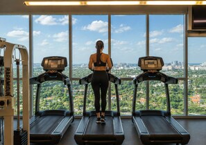 A gym with three treadmills, large windows, and a city view.