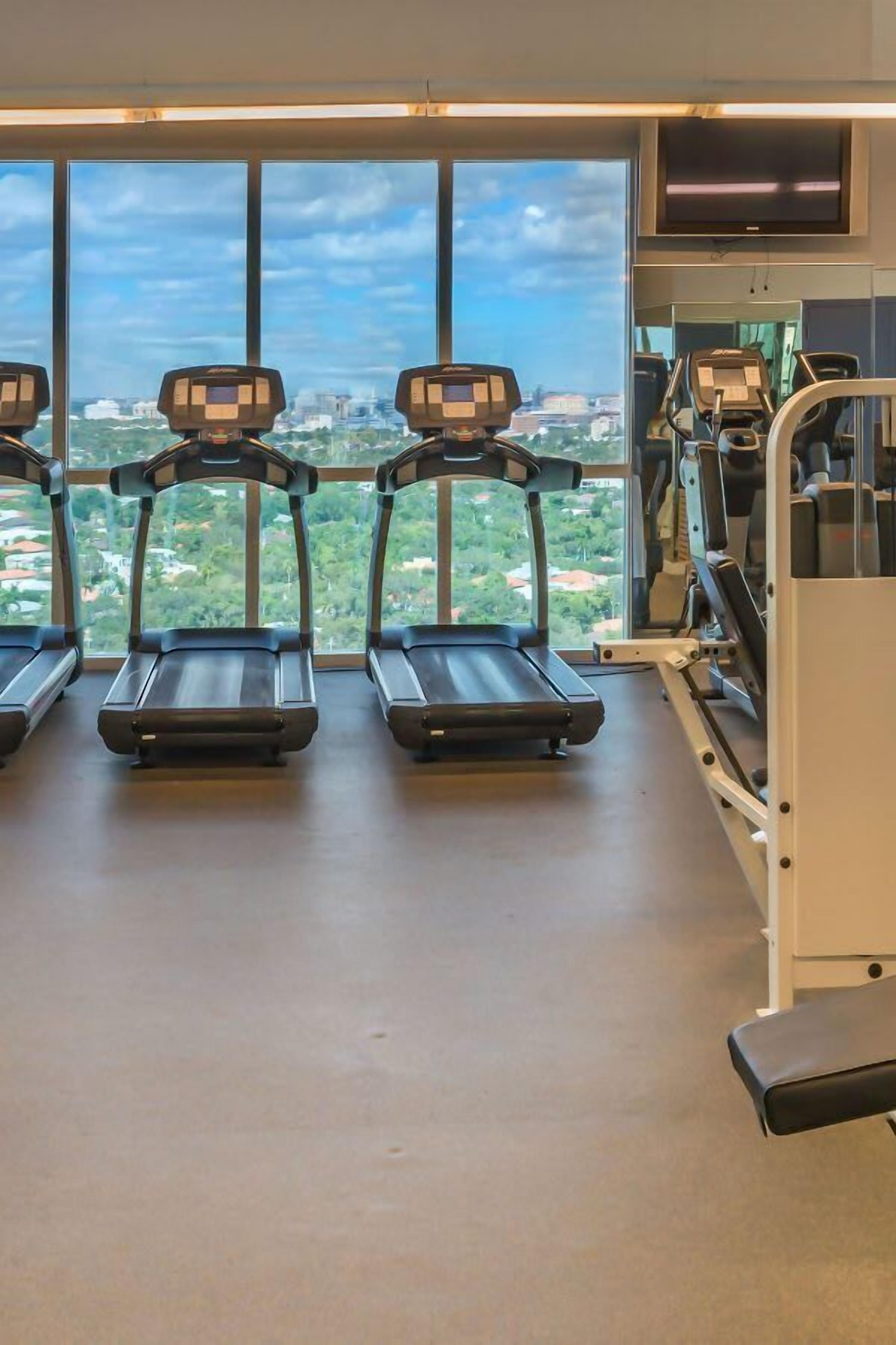 A gym with treadmills, weight machines, and a large window with a city view.