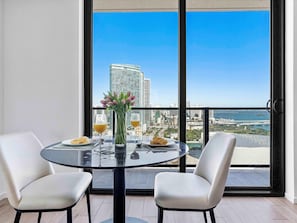 A balcony with a glass table, two chairs, a vase of flowers, and a city view. - Modern Downtown Residence | Walk to Everything (Miami)
