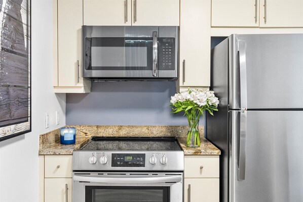 A kitchen with stainless steel appliances, a granite countertop, and light-colored cabinets.