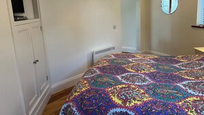 Ein Schlafzimmer mit Bett, Kleiderschrank, Spiegel und einer gerahmten Sammlung kleiner Objekte an der Wand.