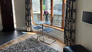 Ein Zimmer mit einem großen Fenster, einem Tisch mit Stühlen, einem Teppich und einer dunklen Holztür.