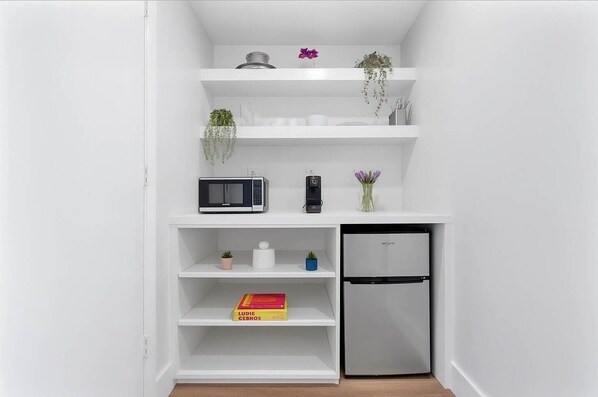 A compact kitchenette with a microwave, coffee maker, and a refrigerator.