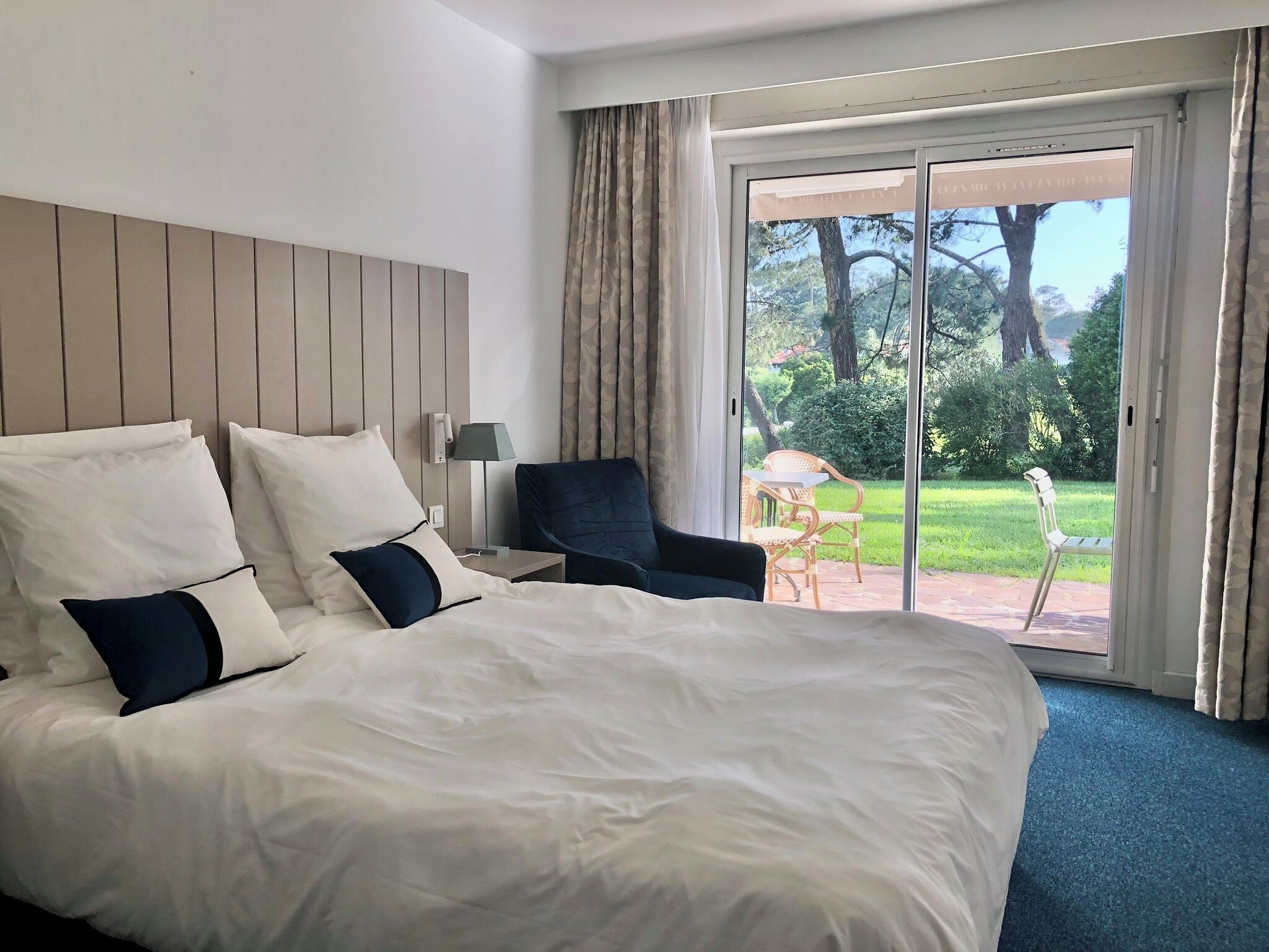 Ein Hotelzimmer mit einem großen Bett, einem Sessel, einem Tisch und einer Schiebetür zu einem Außenbereich.
