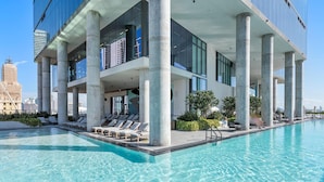 A modern hotel with a rooftop infinity pool, large glass windows, and a view of the city skyline.