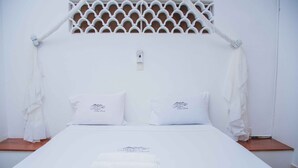 A bed with white bedding and pillows, a white canopy, and a logo on the pillows and bedspread. - Diani Doric Cottages (Diani Beach)