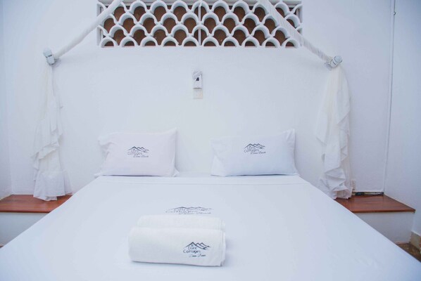 A bed with white bedding and pillows, a white canopy, and a logo on the pillows and bedspread. - Diani Doric Cottages (Diani Beach)