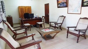 A living room with a wooden desk, two chairs, a coffee table, and a television. - Diani Doric Cottages (Diani Beach)