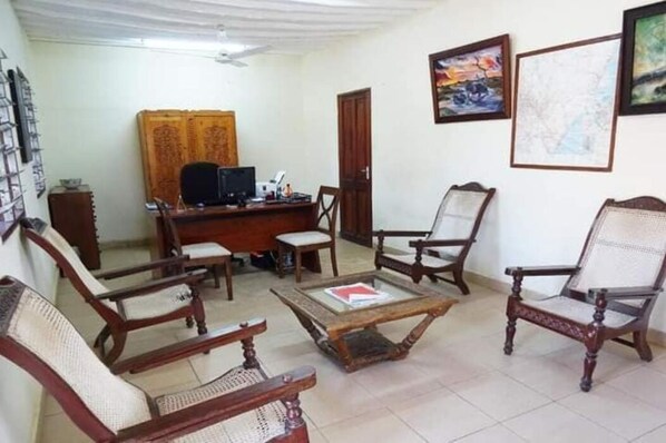 A living room with a wooden desk, two chairs, a coffee table, and a television. - Diani Doric Cottages (Diani Beach)
