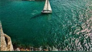 A sailboat on a calm sea with a rocky coastline in the background. - Diani Doric Cottages (Diani Beach)