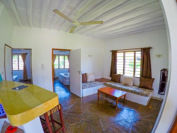 A spacious living area with a sofa set, a wooden table, and a ceiling fan. - Diani Doric Cottages (Diani Beach)