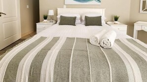 A bedroom with a bed, two bedside tables, a nightstand, a painting, and a door. - Diani Doric Cottages (Diani Beach)