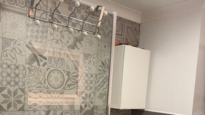 Ένα μπάνιο με διακοσμητικά πλακάκια, ένα ντους με γυάλινη πόρτα, ένας λευκός νιπτήρας και ένα ντουλάπι.