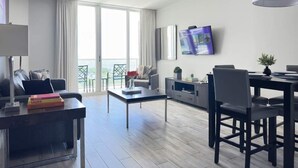 A modern living room with a sofa, coffee table, TV, and dining area. - Modern Studio Suite - Heart of Coconut Grove (Miami)