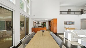 A spacious living area with a large wooden dining table, grey sofas, and a kitchen in the background.