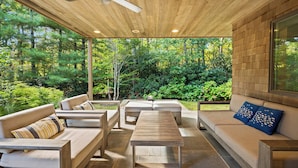 A covered outdoor seating area with wooden furniture and a view of a forested landscape.