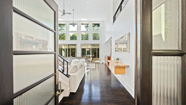 A spacious hallway with a wooden floor, a white sofa, and a dining area with a table and chairs.