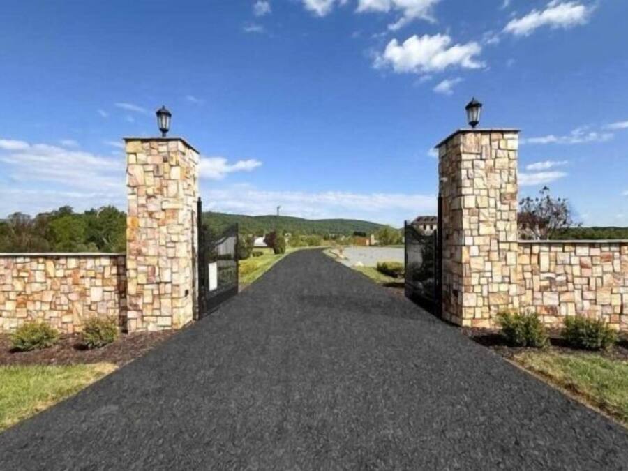 A paved pathway leading to a gated entrance with stone walls and lanterns.