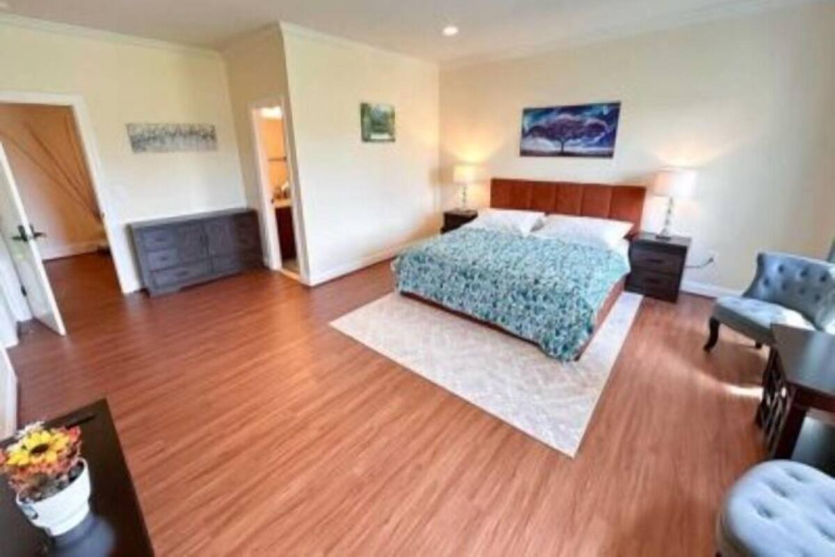 A bedroom with a large bed, a nightstand, a chair, and a painting on the wall.