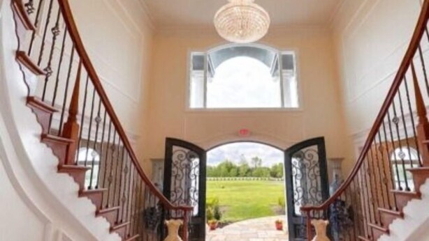 Un'imponente scalinata con un lampadario, che conduce a un'apertura con vista su un giardino.