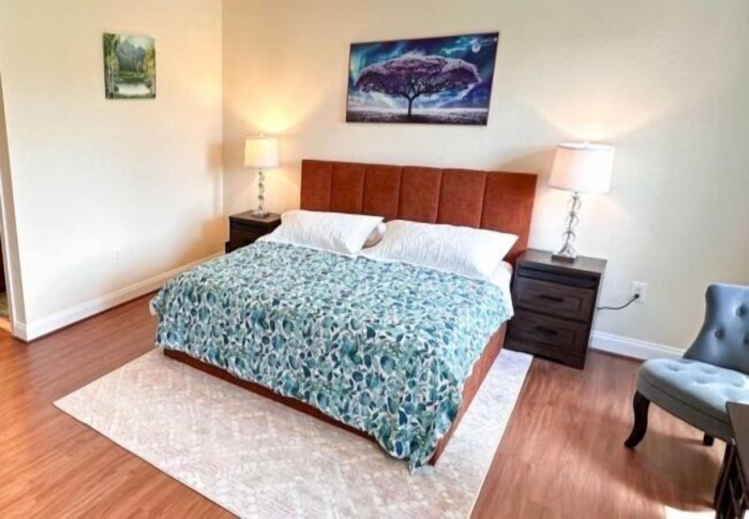 Een slaapkamer met een bed, nachtkastjes, een stoel en kunst aan de muur.