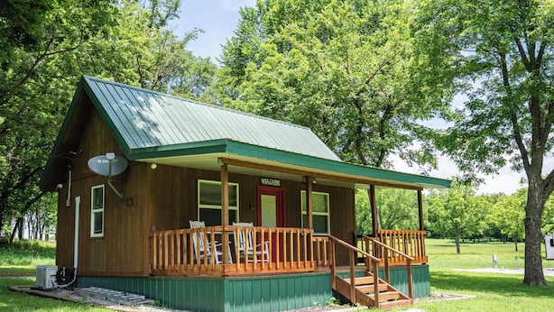 Un piccolo chalet in legno con tetto verde, un portico con ringhiere di legno e una porta rossa.