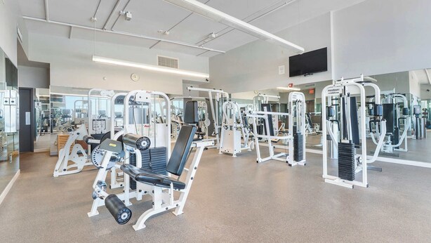 Een moderne sportschool met diverse fitnessapparaten, spiegels en een groot televisiescherm.