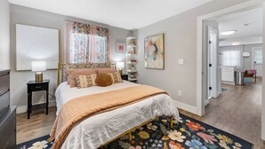A bedroom with a bed, bedside tables, a nightstand, a window with curtains, and a door leading to another room. - Optimist Abode 1: Chic Stay on Greenway, less than 7 min to NoDa-Midwood-Uptown (Charlotte)