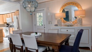 Un comedor con una mesa y sillas de madera, una araña y un espejo decorativo.
