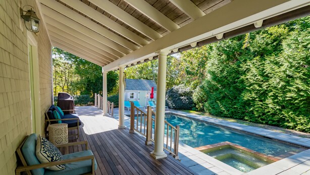 Una terraza de madera con piscina, mobiliario exterior y un área cubierta.