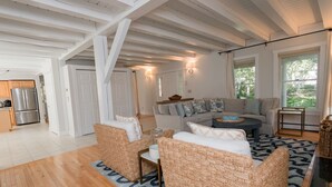 Amplia sala de estar con piso de madera, mobiliario de mimbre, un sofá gris y una mesa de comedor.