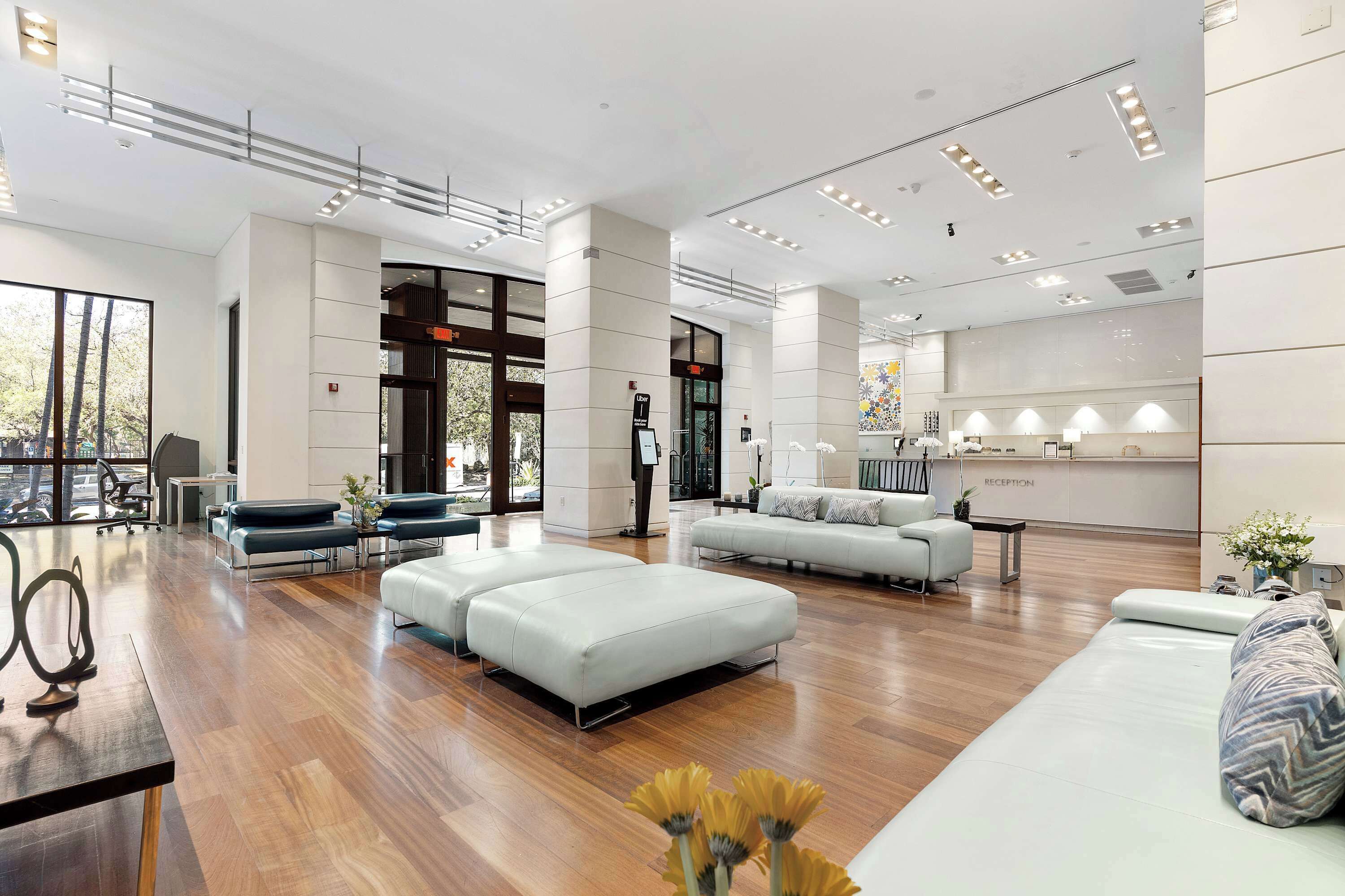 A spacious hotel lobby with a reception desk, seating areas, and a large window offering a view of the outdoors. - Floor-to-Ceiling Glass Residence | Coconut Grove (Miami)