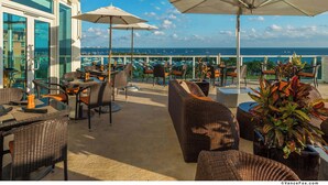 An outdoor terrace with wicker furniture, umbrellas, and potted plants. - Floor-to-Ceiling Glass Residence | Coconut Grove (Miami)