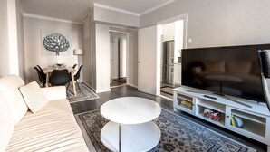 Ein modernes Wohnzimmer mit einer Couch, einem runden Couchtisch, einem Flachbildfernseher und einer Essecke mit Tisch und Stühlen.