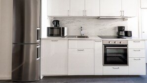 Eine moderne Küche mit weißen Schränken, einem Edelstahl-Kühlschrank, einer Mikrowelle, einer Kaffeemaschine und einem Backofen.