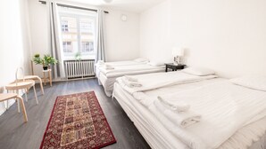 Ein Hotelzimmer mit zwei Betten, einem kleinen Tisch, einem Sessel, einer Heizung und einem Fenster mit Vorhängen.