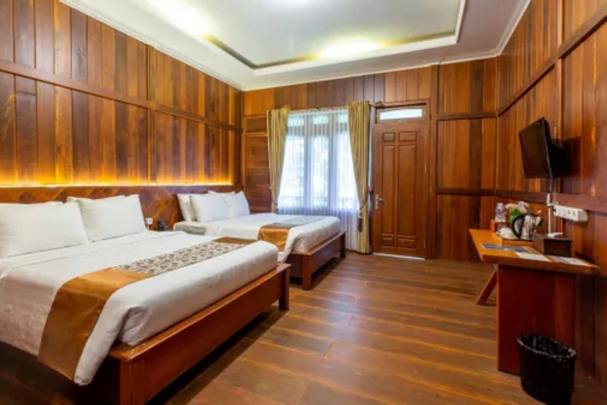 A hotel room with wooden paneling, two beds, a desk, and a TV.